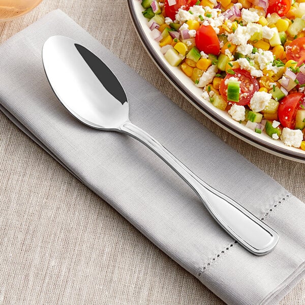 A bowl of salad with Acopa Scottdale serving spoon on a table.