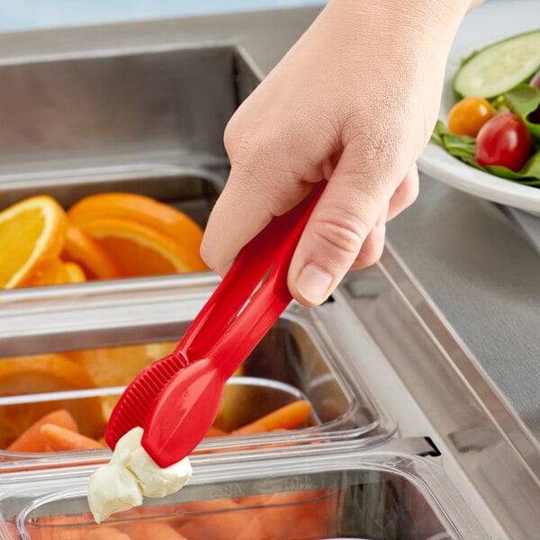 A hand using a Cambro red plastic tongs to serve salad over a container of food.