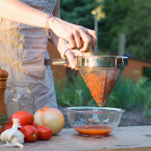 A woman using a Weston stainless steel sieve to strain orange liquid into a bowl.