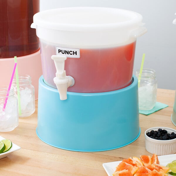 The blue base of a Choice round beverage dispenser on a table with cups and a bowl of blueberries.