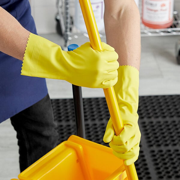 A person wearing yellow Cordova Latex rubber gloves with a yellow mop handle.