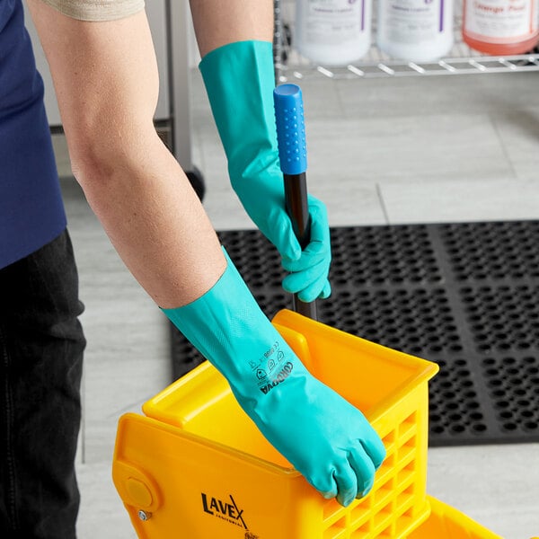 A person wearing Cordova green nitrile gloves holding a yellow mop bucket.