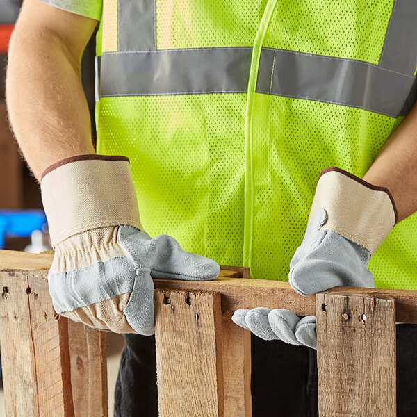 A man wearing Cordova white canvas work gloves with side split leather palms and rubber cuffs holding a piece of wood.