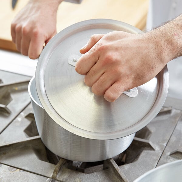 A person's hand holding a Vollrath Arkadia lid over a pot.