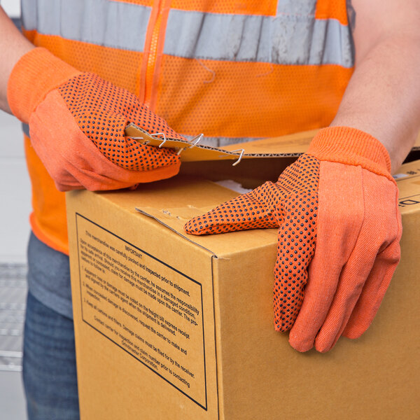 A person wearing Cordova hi-vis orange canvas work gloves with black PVC dots holding a box.