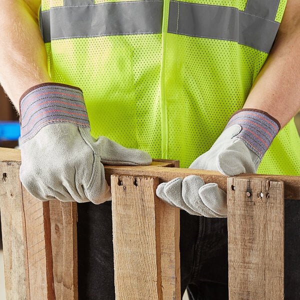 A person wearing Cordova leather work gloves holding a piece of wood.