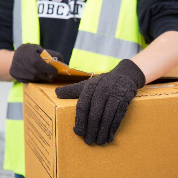 A person wearing Cordova brown cotton jersey gloves holding a box.