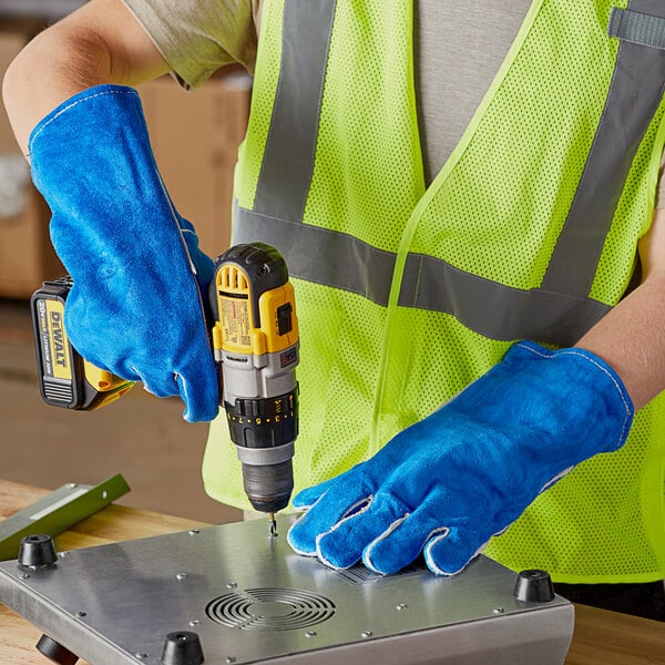 A man in a safety vest using Cordova blue leather gloves to operate a drill.