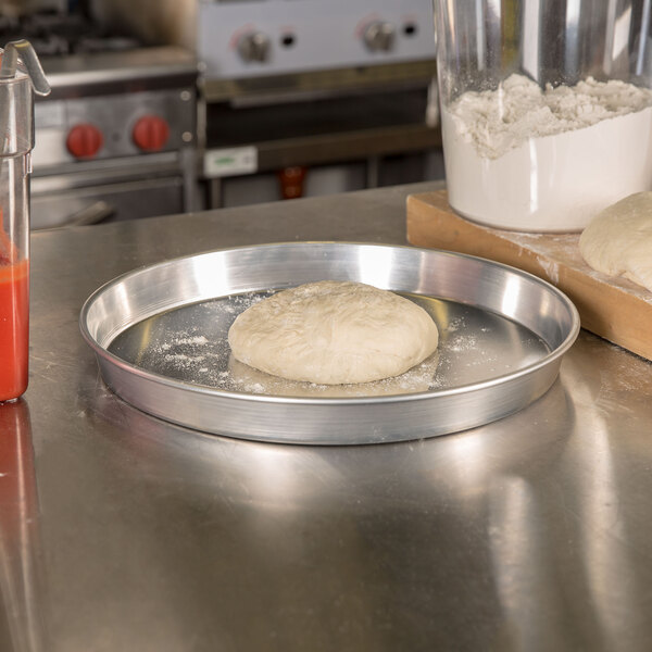 An American Metalcraft aluminum pizza pan with dough on it.