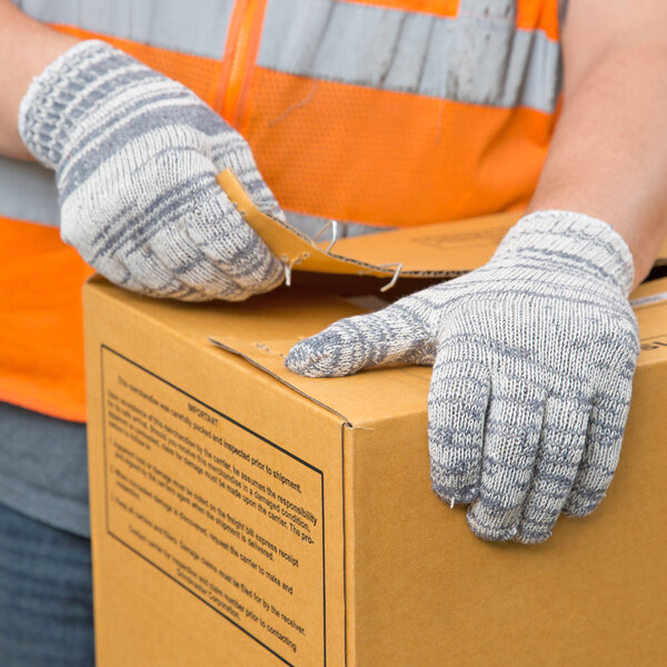 A person wearing Cordova heavy weight multi-color jersey work gloves holding a box.