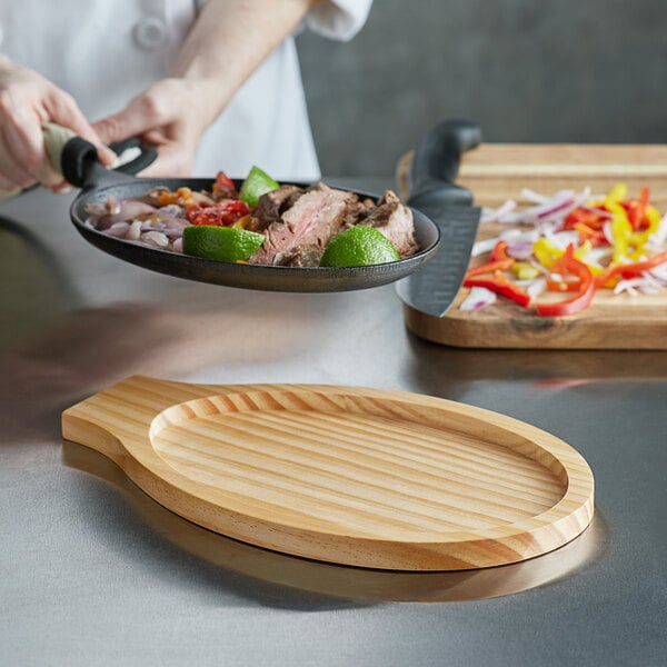 A chef using a Choice oval pine wood underliner to prepare food on a wooden cutting board.