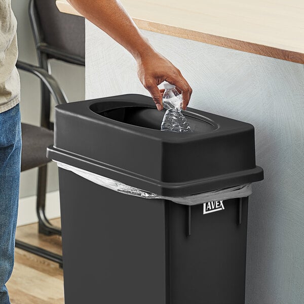 A person putting a plastic bag into a Lavex Black Slim Rectangular Trash Can.