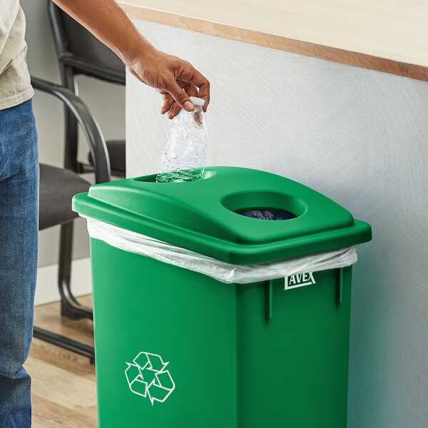 A person putting a plastic bottle into a green Lavex Slim Recycling trash can.