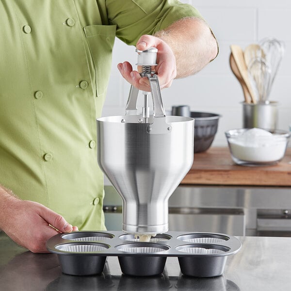 A person using a Choice aluminum batter dispenser to fill a cupcake tin.