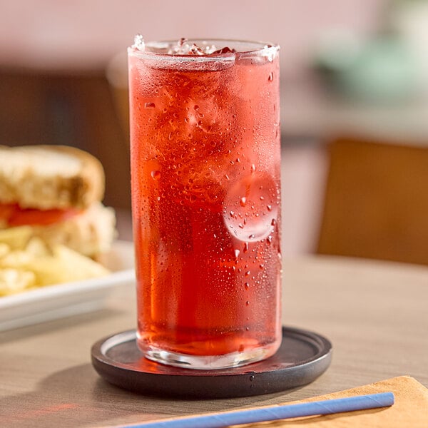 A tall glass of red cranberry juice with ice on a coaster.