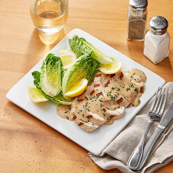 An Acopa bright white square plate with a fork and knife on a table with a glass of water.