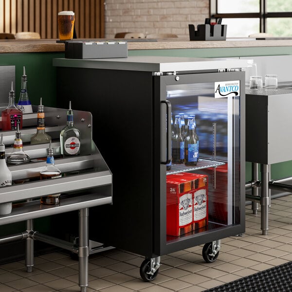 An Avantco black glass door back bar refrigerator on a counter with bottles of beer inside.