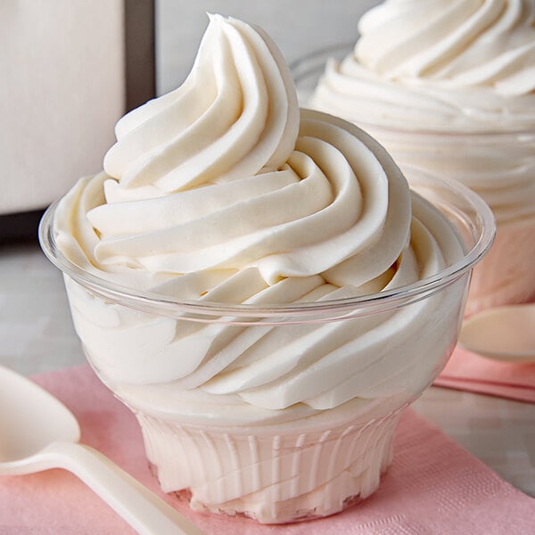 A close up of a clear plastic dessert cup filled with swirly white ice cream with a spoon.