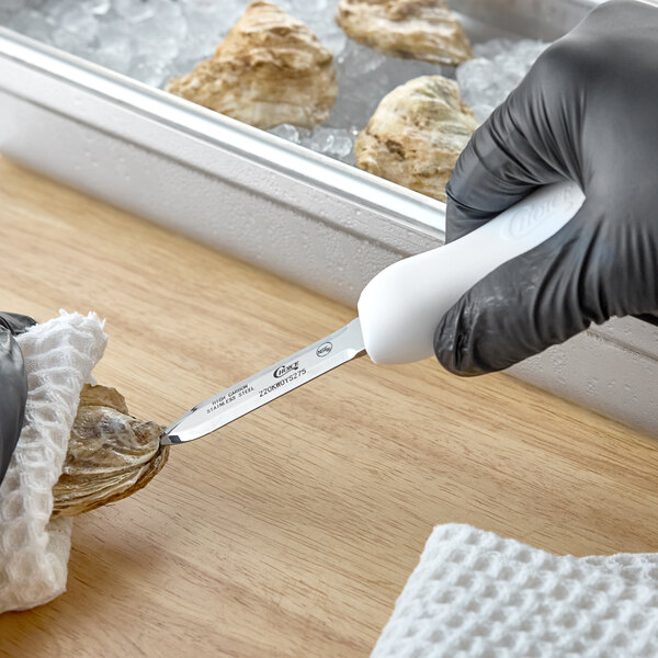 An oyster knife with a white handle being used to open an oyster.