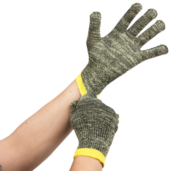 A pair of Cordova Camo Cut Resistant gloves with yellow and black stripes on the cuffs being worn by a pair of hands.