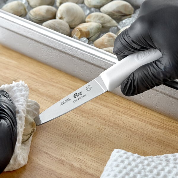 A stainless steel clam knife with a white handle being used to open a clam.