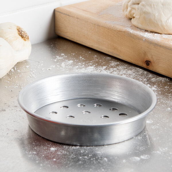 An American Metalcraft standard weight aluminum pizza pan with dough in it on a counter.