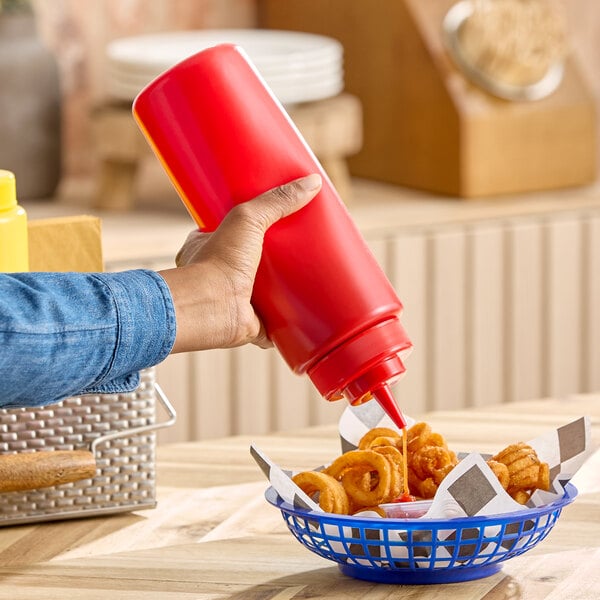 A large red squeeze bottle being used to dispense sauce onto a basket of curly fries.