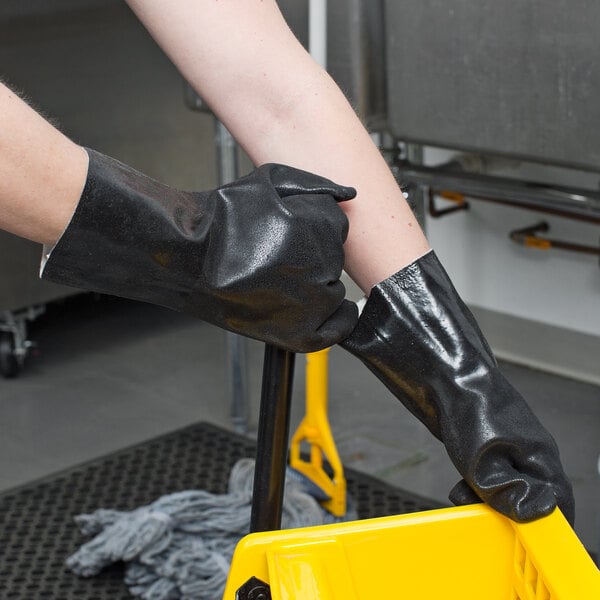 A pair of hands wearing Cordova black rubber gloves with a yellow bucket.