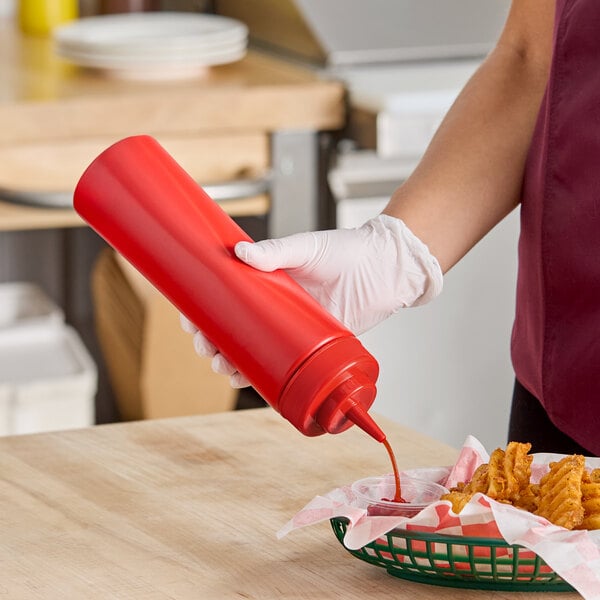 A red 24 oz. wide mouth squeeze bottle being used to dispense sauce onto food.
