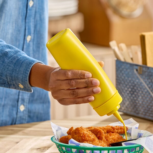 A yellow 12 oz. wide mouth squeeze bottle being used to dispense sauce onto fried food.