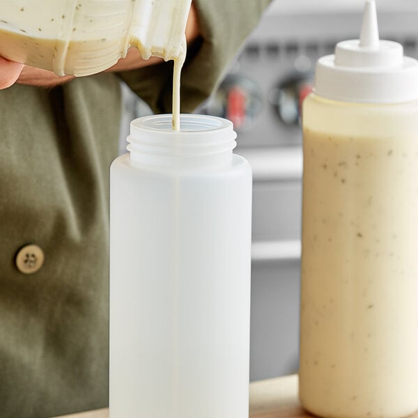 A person using a Choice clear wide mouth squeeze bottle to pour white liquid into a plastic container.