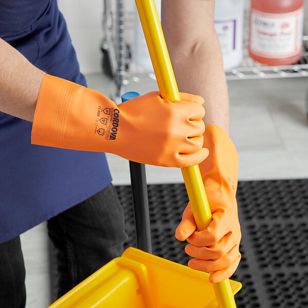 A person wearing orange Cordova rubber gloves holding a yellow pole.