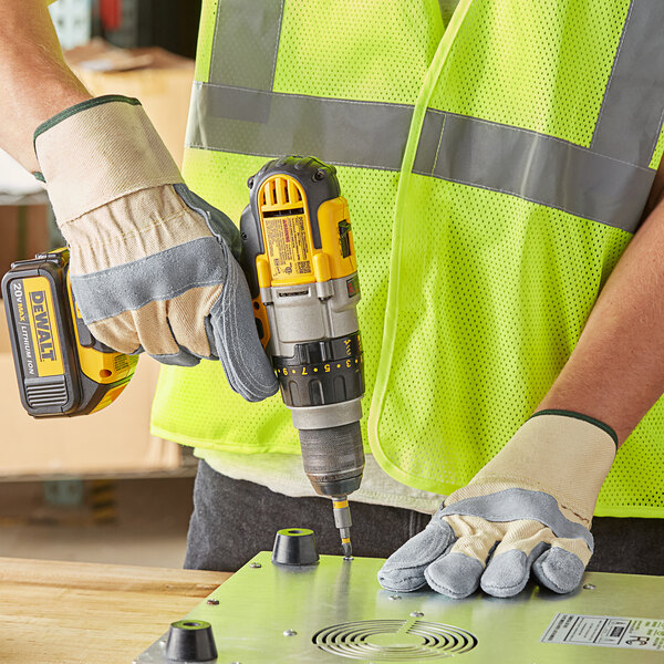 A man wearing Cordova white canvas work gloves with leather palms and rubber cuffs using a drill.