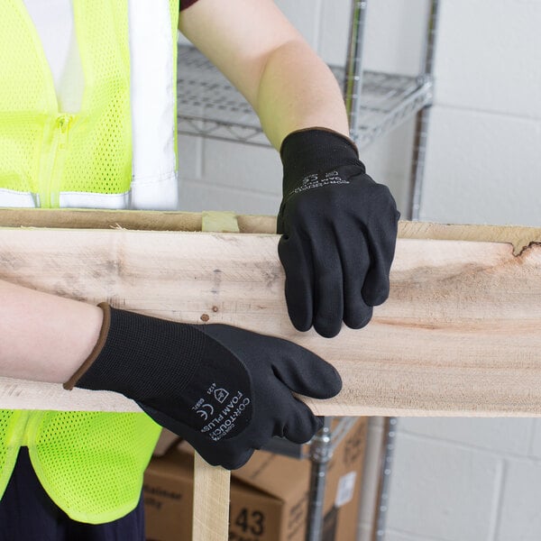 A person wearing Cordova black safety gloves with black foam nitrile/polyurethane coating holding a piece of wood.