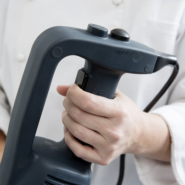 A hand holding a black switch cover for an AvaMix immersion blender.