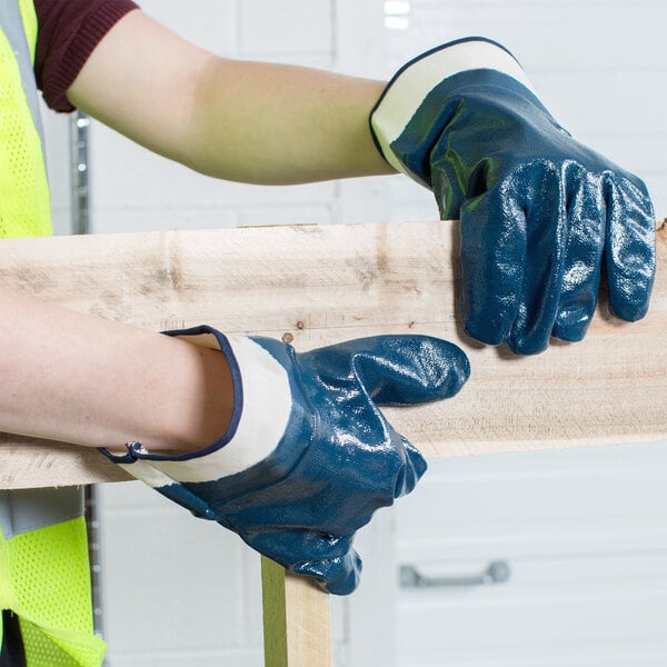 A person wearing Cordova rough supported nitrile gloves holding a piece of wood.