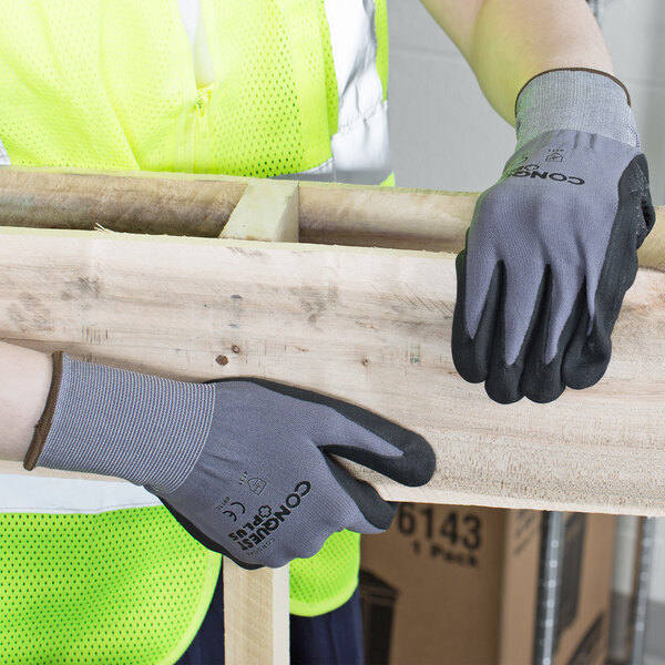 A person wearing Cordova Conquest Plus safety gloves holding a piece of wood.