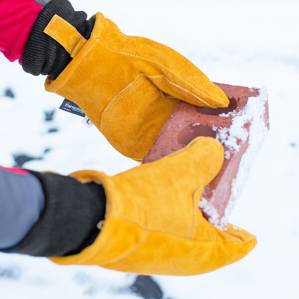 A person wearing Cordova russet leather freezer mittens holding a brick.