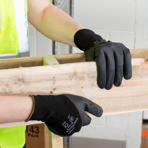 A person wearing Cordova black gloves with nitrile dots holding a piece of wood.