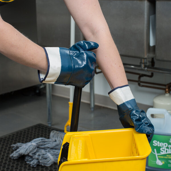 A person wearing Cordova smooth supported nitrile gloves holding a yellow bucket.
