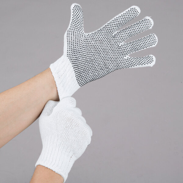 A person wearing Cordova white work gloves with black dots on the palm.
