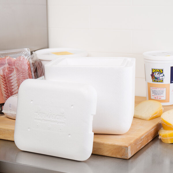 A white foam Nordic insulated container next to cheese and meat on a table.