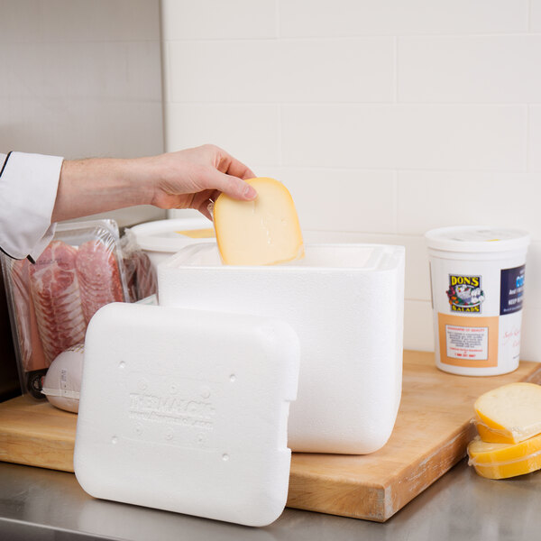 A hand putting a piece of cheese into a white styrofoam container.
