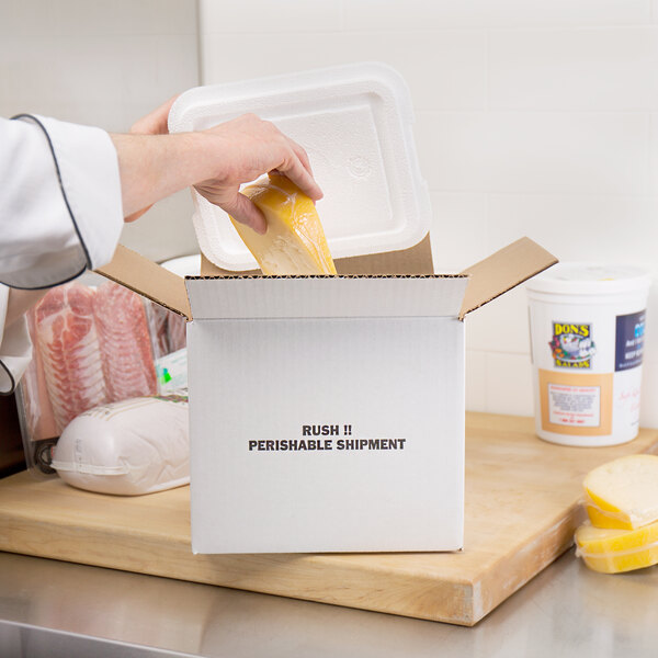 A hand putting cheese into a white Nordic insulated shipping box.