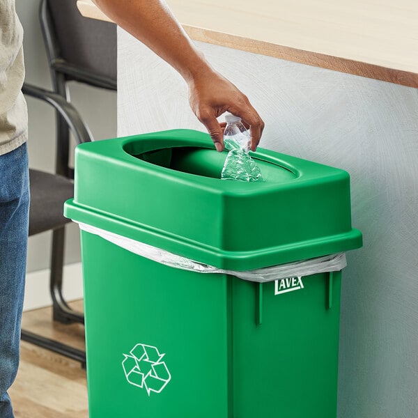 A person using a hand to put a plastic bottle into a green Lavex Slim Rectangular Trash Can.