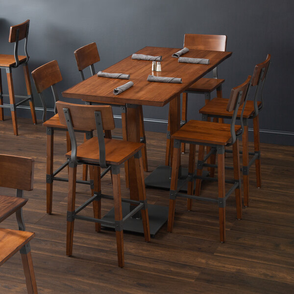 A Lancaster Table & Seating wooden bar height table with chairs and napkins.