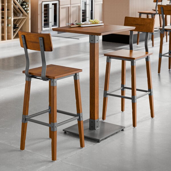 A bar height table set with a square rustic walnut finish wood table and two matching bar stools featuring metal accents.