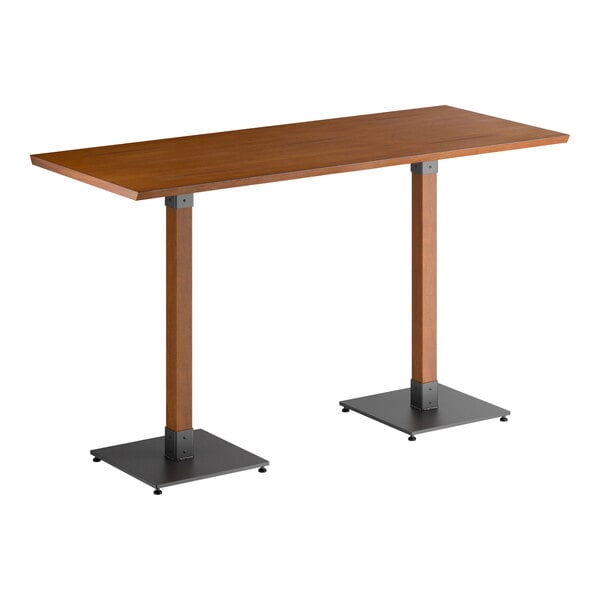 A rectangular bar-height table with a solid wood top in a walnut finish, supported by two square wooden legs with black metal bases.