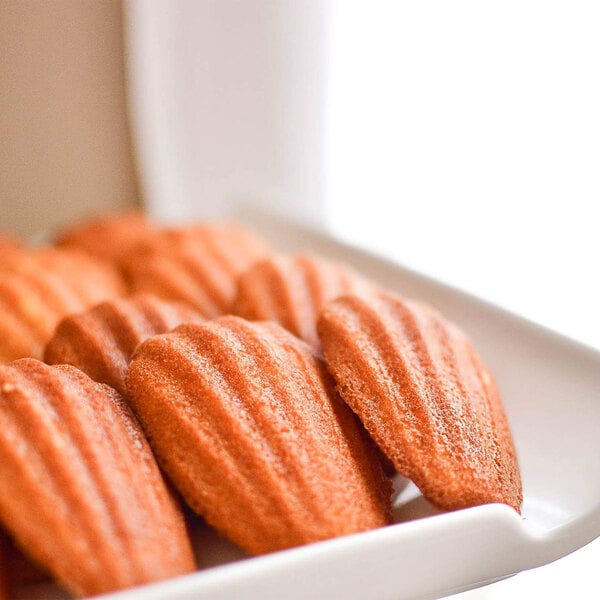 A white plate with a group of brown and orange Madeleine cookies.