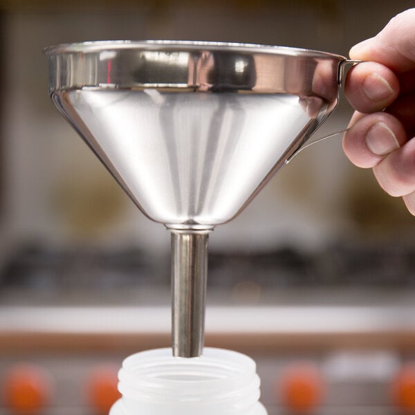 A hand using a Matfer Bourgeat stainless steel funnel to pour liquid into a plastic container.